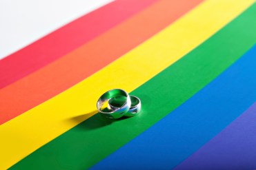 Two silver rings resting on a background in colors of a homosexual flag
