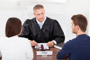 Rear view of couple with judge writing at desk in court